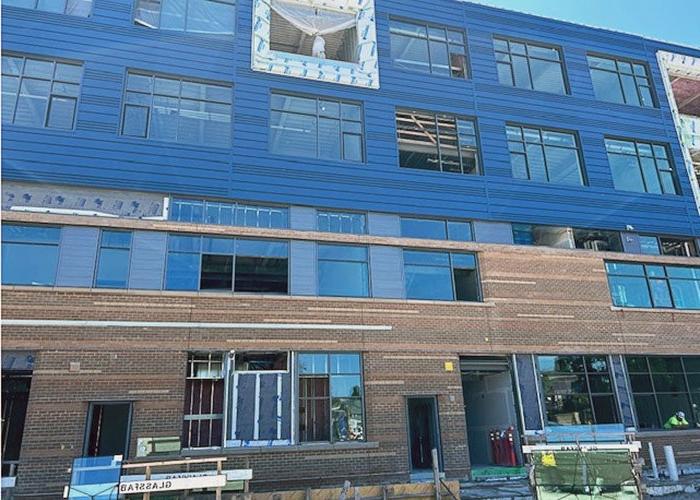 part of a 4-story building under construction with multiple windows. the top two floors have blue metal paneling, there is brick on the other two floors